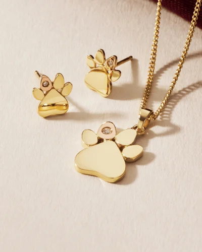 Clogau gold paw-print pendant and earrings on a cream backdrop